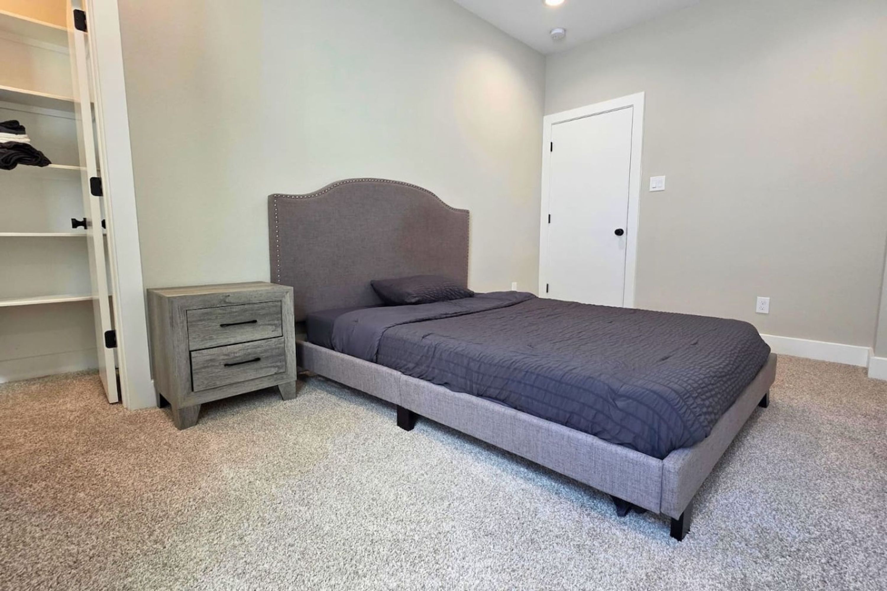 A bedroom with a bed, a nightstand, a dresser, and a closet.