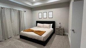 Um quarto com uma cama, uma mesinha de cabeceira, uma prateleira na parede e uma porta.