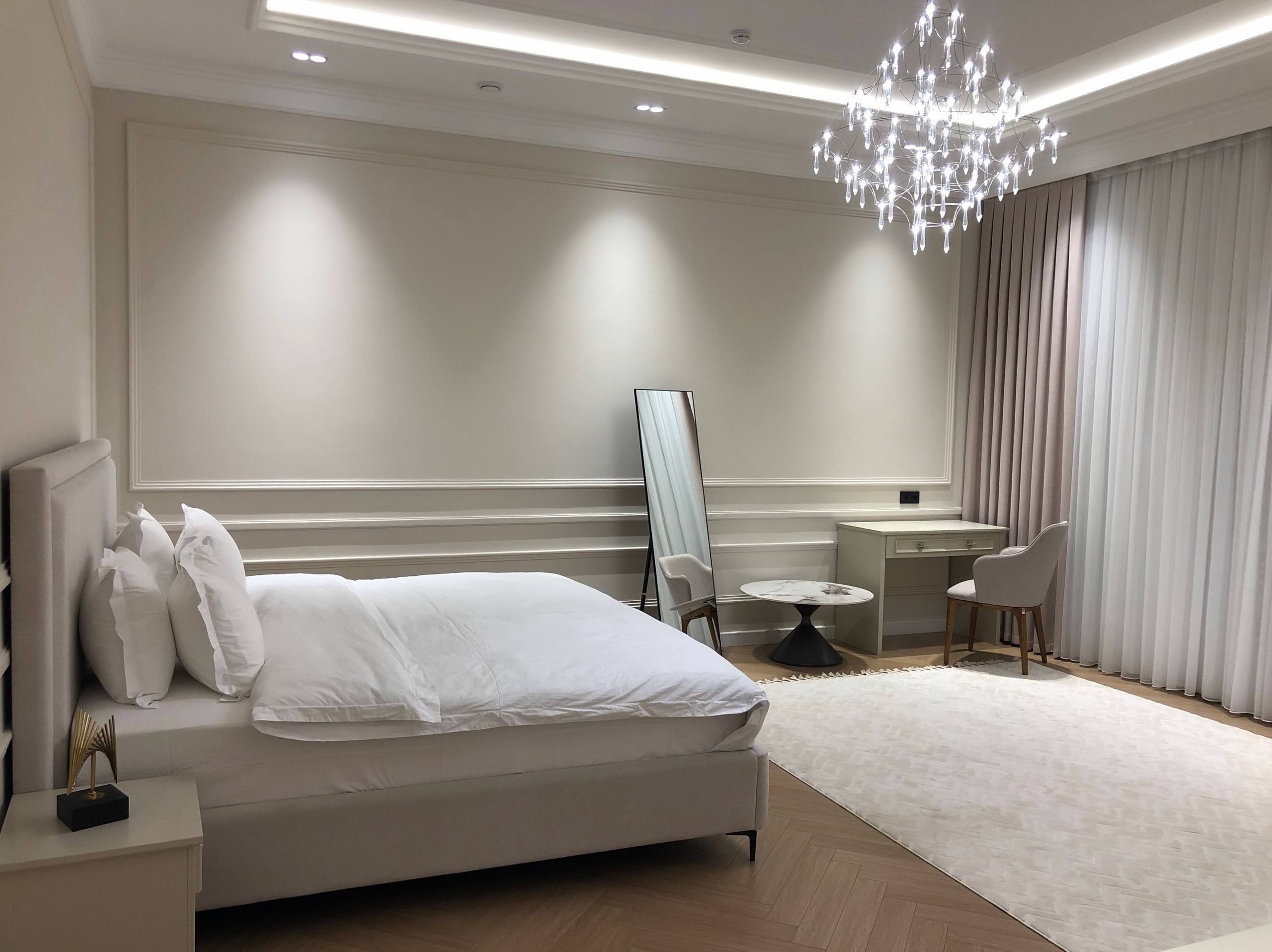 A modern hotel room with a large bed, a small round table, a chair, and a desk.