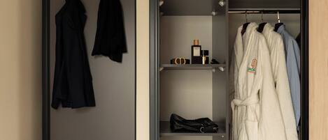 A walk-in closet with hanging clothes, shelves with toiletries, and a suitcase on the floor.