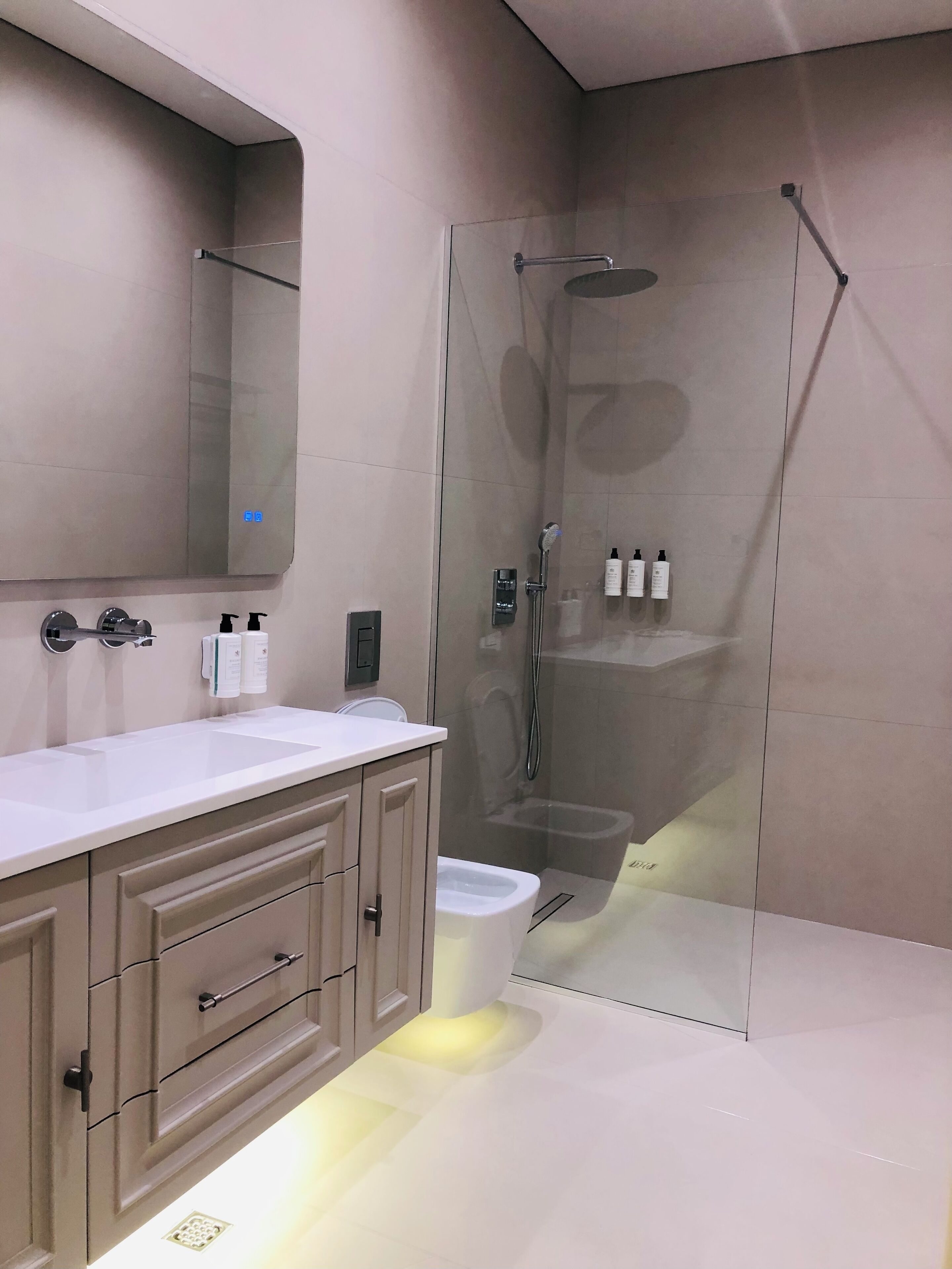 A modern bathroom with a glass-enclosed shower, a white sink, and beige cabinets.