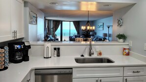 A modern kitchen with a dishwasher, coffee machine, and a large window overlooking the ocean. - Roomy Oceanfront 2/2 condo with Million Dollar views in fabulous Daytona Beach!! (Daytona Beach)
