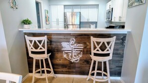 A kitchen with white cabinets, a stainless steel refrigerator, and a wooden island with two bar stools. - Roomy Oceanfront 2/2 condo with Million Dollar views in fabulous Daytona Beach!! (Daytona Beach)
