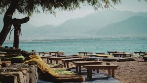 Una spiaggia con tavoli e panche di legno, alcune con cuscini.