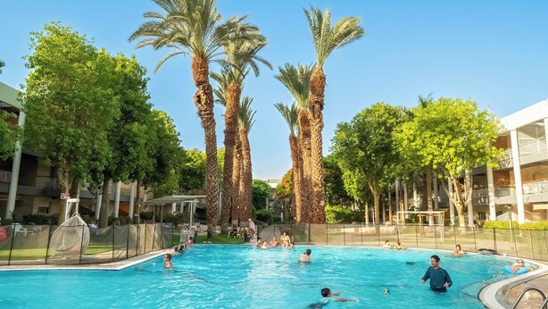 Una piscina circondata da palme e un edificio a più piani con balconi.