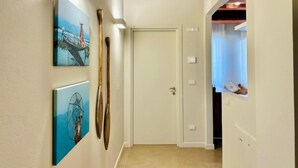 Een gang met een houten plafond, een witte deur en twee kunstwerken in een lijst aan de muur.