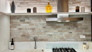 Een moderne keuken met een metselwerk spatwand, een roestvrijstalen afzuigkap en een gasfornuis.
