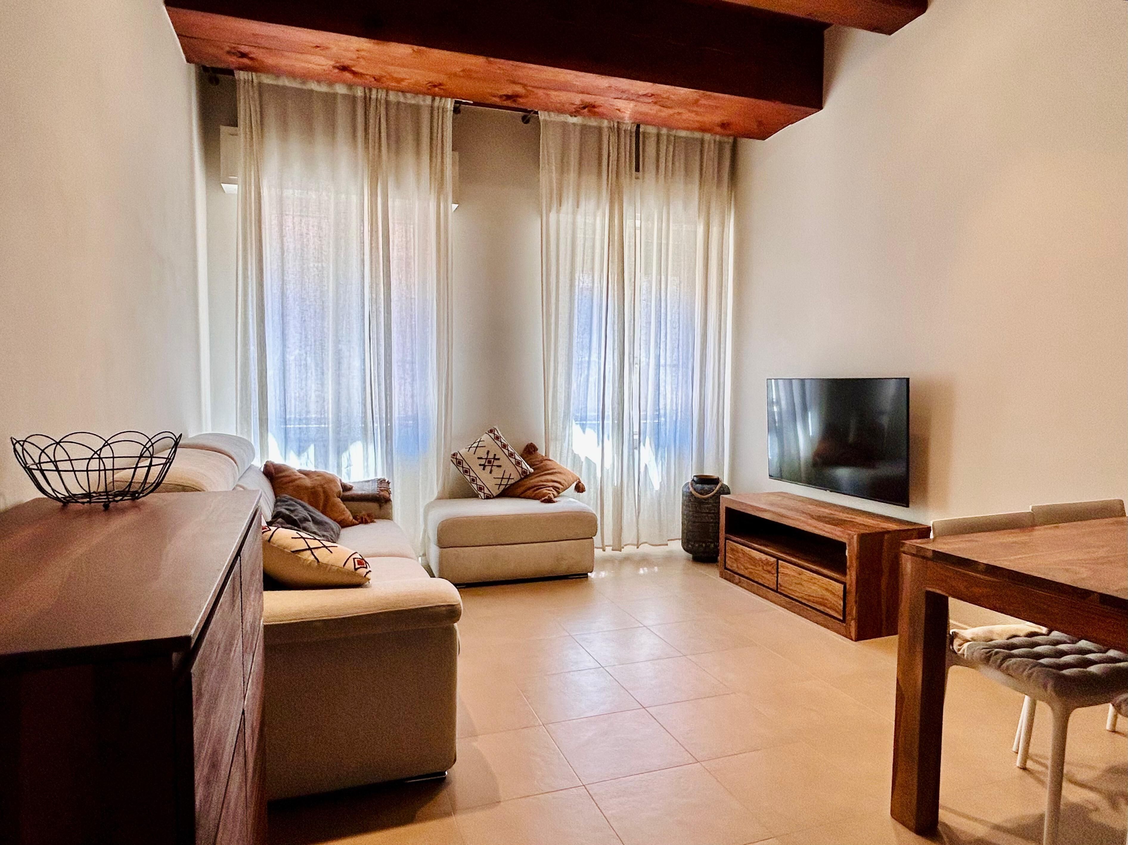 A living room with a sofa, ottoman, TV, and wooden dining table.