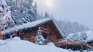 Una cabaña de madera con techo inclinado, rodeada de árboles cubiertos de nieve y un cielo despejado.