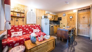 Una habitación acogedora con un sofá rojo, una mesa de comedor de madera, una zona de cocina y una puerta de madera.