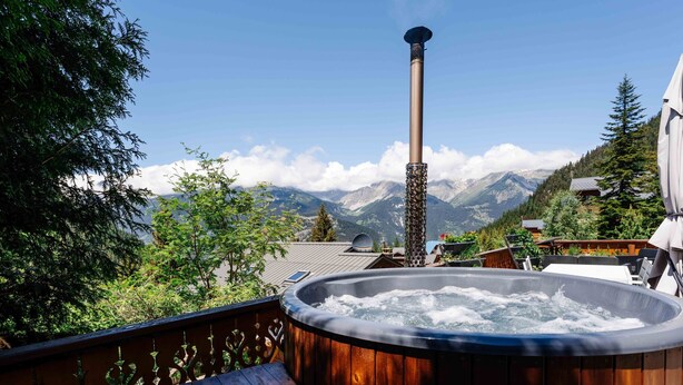 Un jacuzzi en una terraza de madera con vista a la montaña, una chimenea y una barandilla de madera.