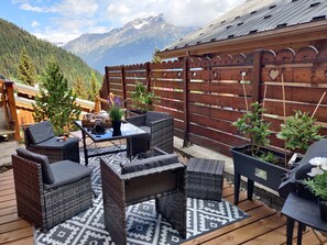 Una terraza de madera con mobiliario de mimbre, un tapete estampado y plantas en macetas.