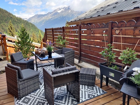 A wooden deck with wicker furniture, a patterned rug, and potted plants.. 'Bas De Lout'Chi Valfréjus' Apartment with Mountain View, Private Terrace and Wi-Fi