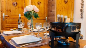 Una mesa de comedor de madera con platos, cubiertos, copas de vino y un florero con flores.