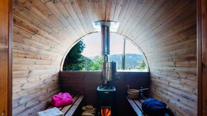 Un sauna con estufa de leña, bancos y vistas al exterior.