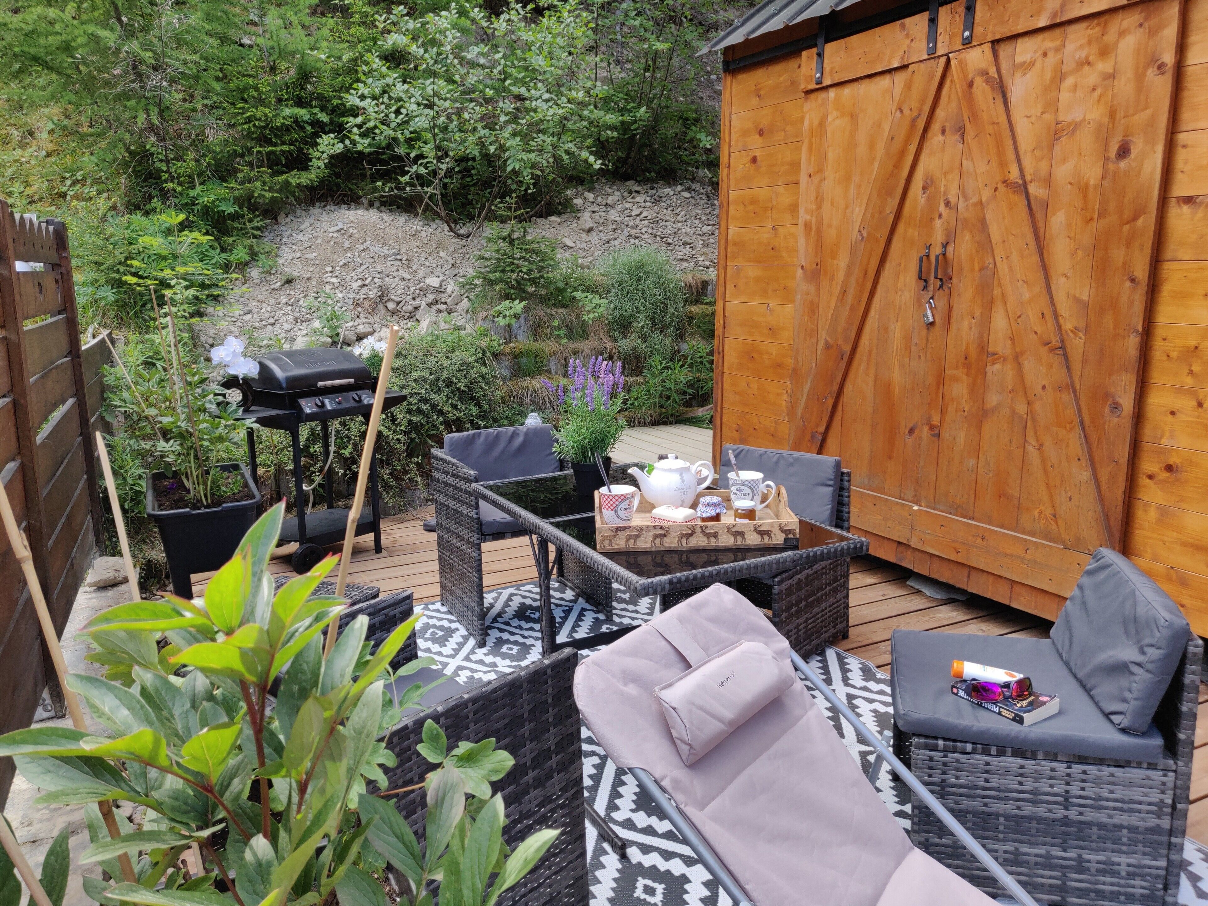 Un patio con mobiliario de mimbre, una parrilla y un cobertizo de madera.