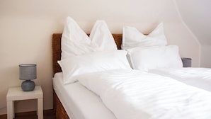 A neatly made bed with white bedding and pillows, a wooden headboard, and a small bedside table with a lamp.