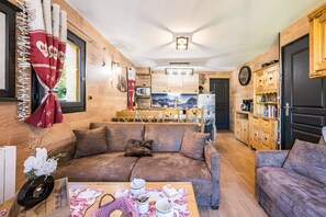 Una sala de estar acogedora con un sofá, una mesa de centro con adornos y una zona de cocina con armarios de madera y un refrigerador.