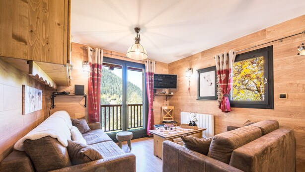 A wooden cabin interior with a sofa, a table, a TV, and a window with curtains. - Apartment 'Chalet Refuge Loup Blanc Valfréjus' with Mountain View, Balcony and Wi-Fi (Valfréjus)