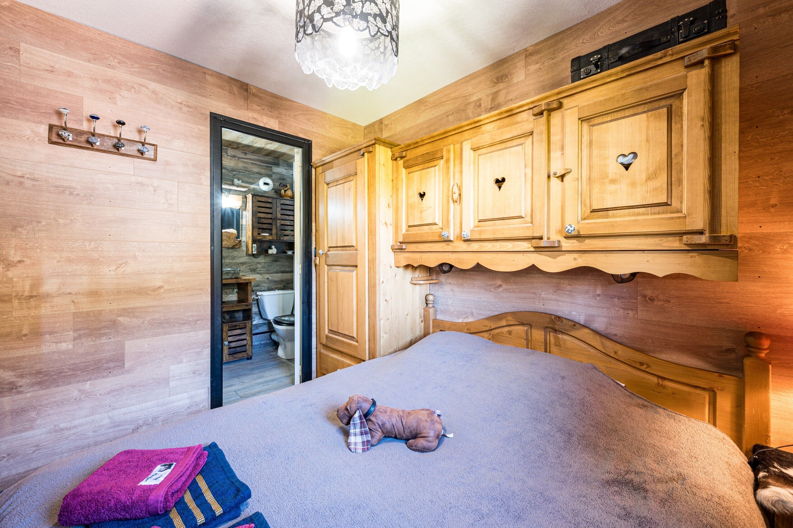 A bedroom with a bed, a wooden headboard, a teddy bear, and a mirror.