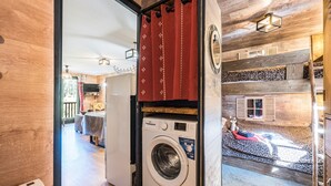 A laundry room with a washing machine, a red curtain, and a bed with a leopard print blanket. - Apartment 'Chalet Refuge Loup Blanc Valfréjus' with Mountain View, Balcony and Wi-Fi (Valfréjus)