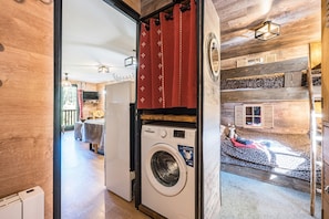 Une buanderie équipée d’un lave-linge, avec un rideau rouge et un lit recouvert d’une couverture à motifs léopard.