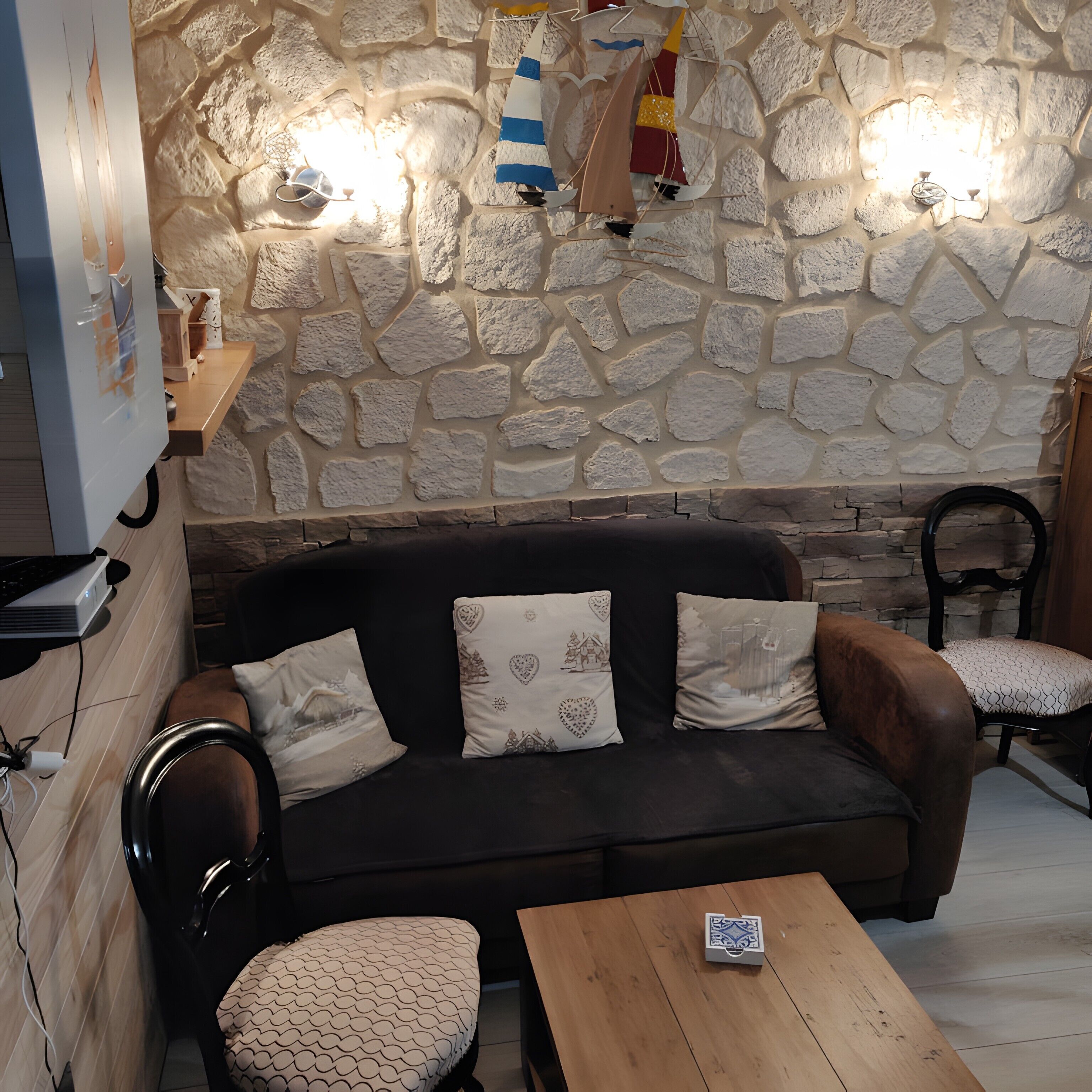 A cozy room with a stone wall, a dark brown sofa with patterned cushions, a wooden table, and a chair.