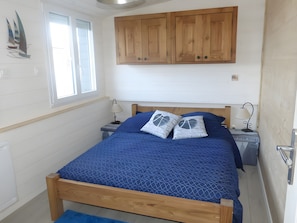 Une chambre à coucher avec un lit en bois, deux tables de chevet, une fenêtre et une armoire en bois.