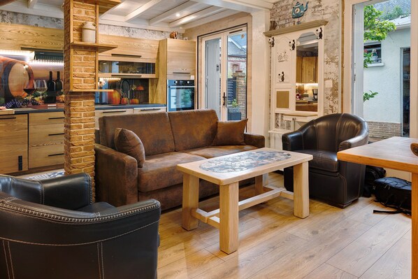 Un espacio de sala acogedor con un sofá de cuero marrón, una mesa de centro de madera y una mesa de comedor con una silla de cuero negro.