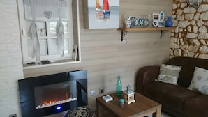 Una sala de estar con chimenea, televisor, pared de piedra, estante de madera con adornos y sofá de cuero marrón.