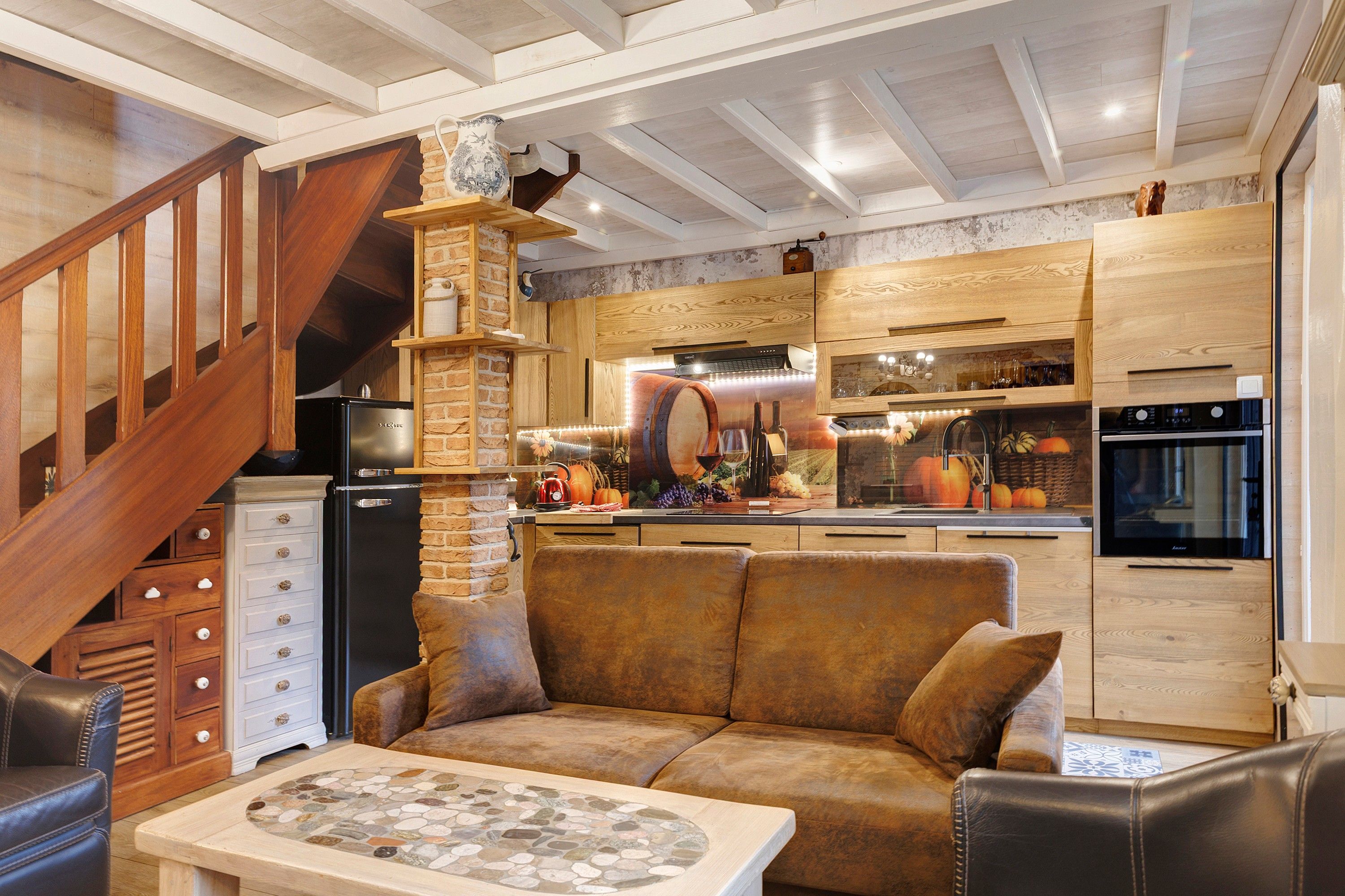 Een gezellige keuken met een stenen open haard, houten keukenkastjes en een moderne koelkast.