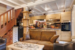 A cozy kitchen with a stone fireplace, wooden cabinets, and a modern refrigerator.