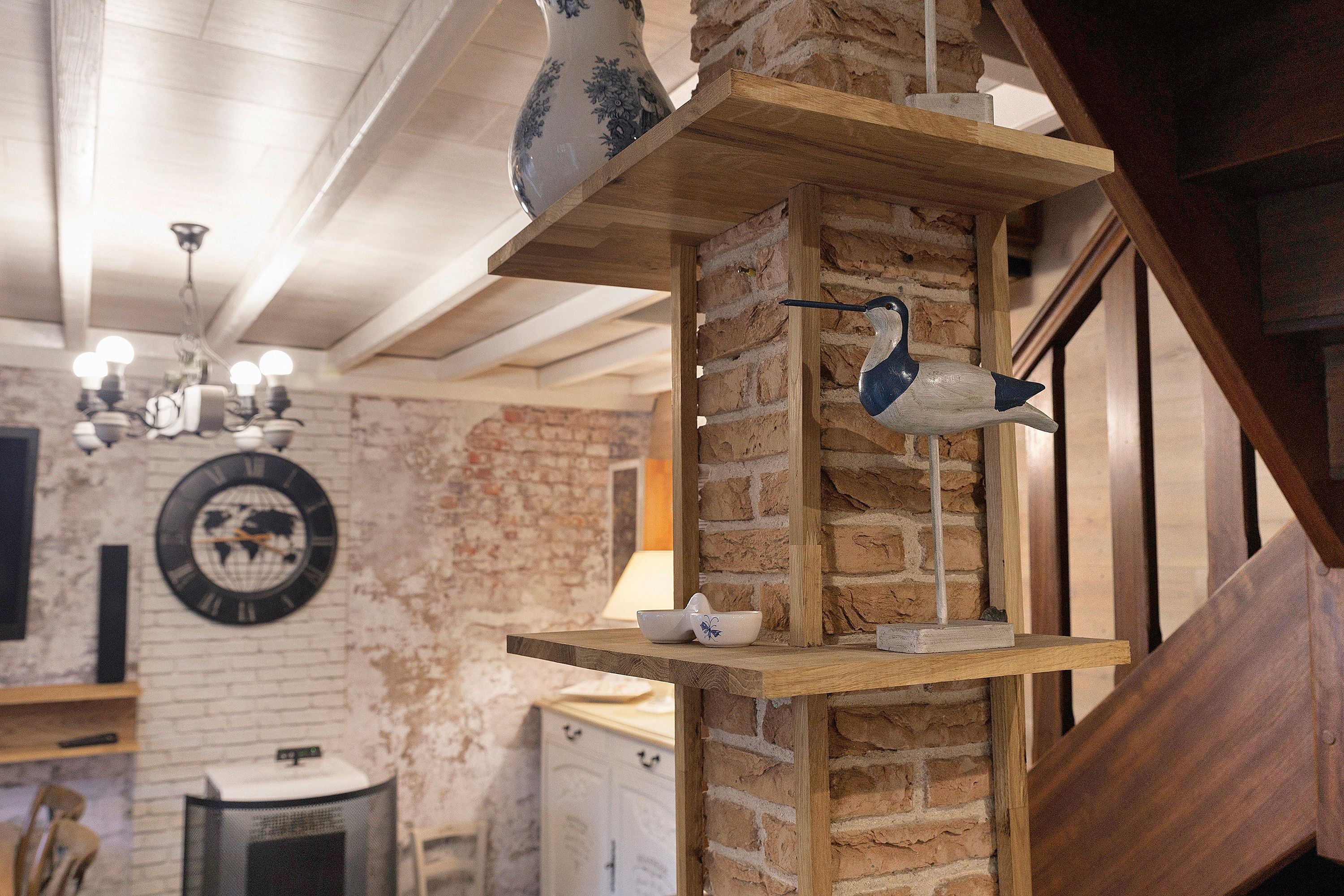 Een rustiek interieur met blootgelegde bakstenen muren, houten balken en een decoratieve vogel op een plank.