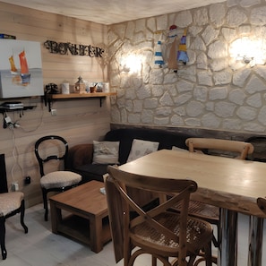 Une pièce chaleureuse avec un mur en pierre, des meubles en bois, une télévision et une étagère ornée d’objets décoratifs.