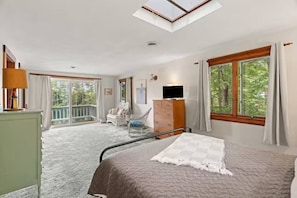 A bedroom with a bed, a dresser, a television, a chair, and a balcony with a view of trees. - Merrymeeting Lake Private Beach, Gazebo & Hot Tub (New Durham)