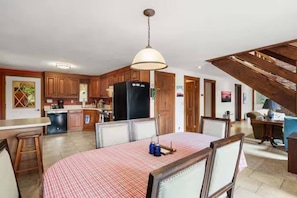 A spacious kitchen with wooden cabinets, a dining table with chairs, a refrigerator, and a hanging light fixture. - Merrymeeting Lake Private Beach, Gazebo & Hot Tub (New Durham)