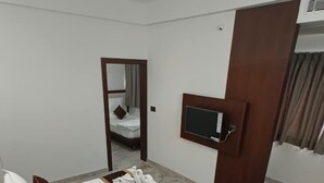 A hotel room with a large bed, a TV mounted on the wall, a wooden headboard, and a mirror above the bed. - Sree Brewery and kitchen (Anekal)