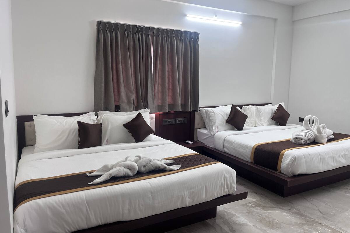A hotel room with two beds, each with white bedding and brown accents, a large window with curtains, and a flat-screen TV on a wooden stand.