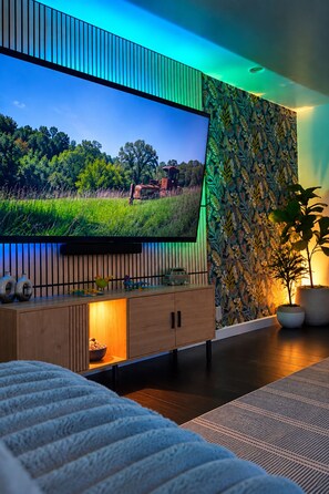 A modern living room with a flat-screen TV, wooden cabinet, and a patterned wall. - Endless Summer, Pool/Theatre/Boat Parking/Walk to London Bridge! (Lake Havasu City)