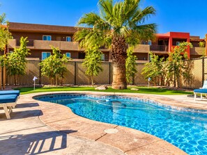 A swimming pool with a curved edge, surrounded by a tiled deck. There are lounge chairs and a palm tree in the foreground. - Endless Summer, Pool/Theatre/Boat Parking/Walk to London Bridge! (Lake Havasu City)