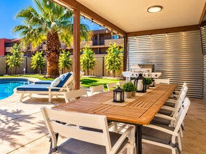 A poolside area with a wooden table and chairs, lounge chairs, and a barbecue grill. - Endless Summer, Pool/Theatre/Boat Parking/Walk to London Bridge! (Lake Havasu City)
