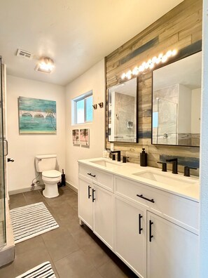 A modern bathroom with a white toilet, double sinks, and a large mirror. - Endless Summer, Pool/Theatre/Boat Parking/Walk to London Bridge! (Lake Havasu City)