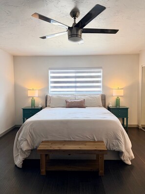 A bedroom with a bed, two bedside tables with lamps, a ceiling fan, a window with blinds, and a wooden bench. - Endless Summer, Pool/Theatre/Boat Parking/Walk to London Bridge! (Lake Havasu City)