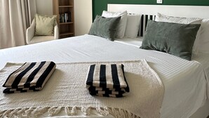 A neatly made bed with striped blankets, a green wall, a wooden bookshelf, and a chair with a cushion.