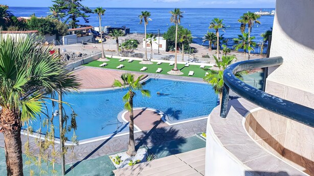 A pool area with a view of the ocean, palm trees, and lounge chairs.