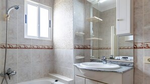 A bathroom with a bathtub, a sink, a mirror, and a showerhead.