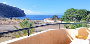 A coastal view with a building, palm trees, and a rocky beach. - Vacation Apartment 'Costamar Oceanview 1 Bed' with Sea View, Shared Pool and Wi-Fi (Los Cristianos)