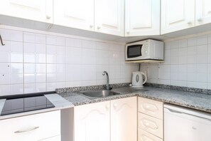 Una cocina con armarios blancos, encimera de granito, pileta de acero inoxidable, microondas y cafetera.