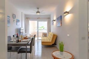 A modern dining area with a table set for two, a sofa, and a ceiling fan.