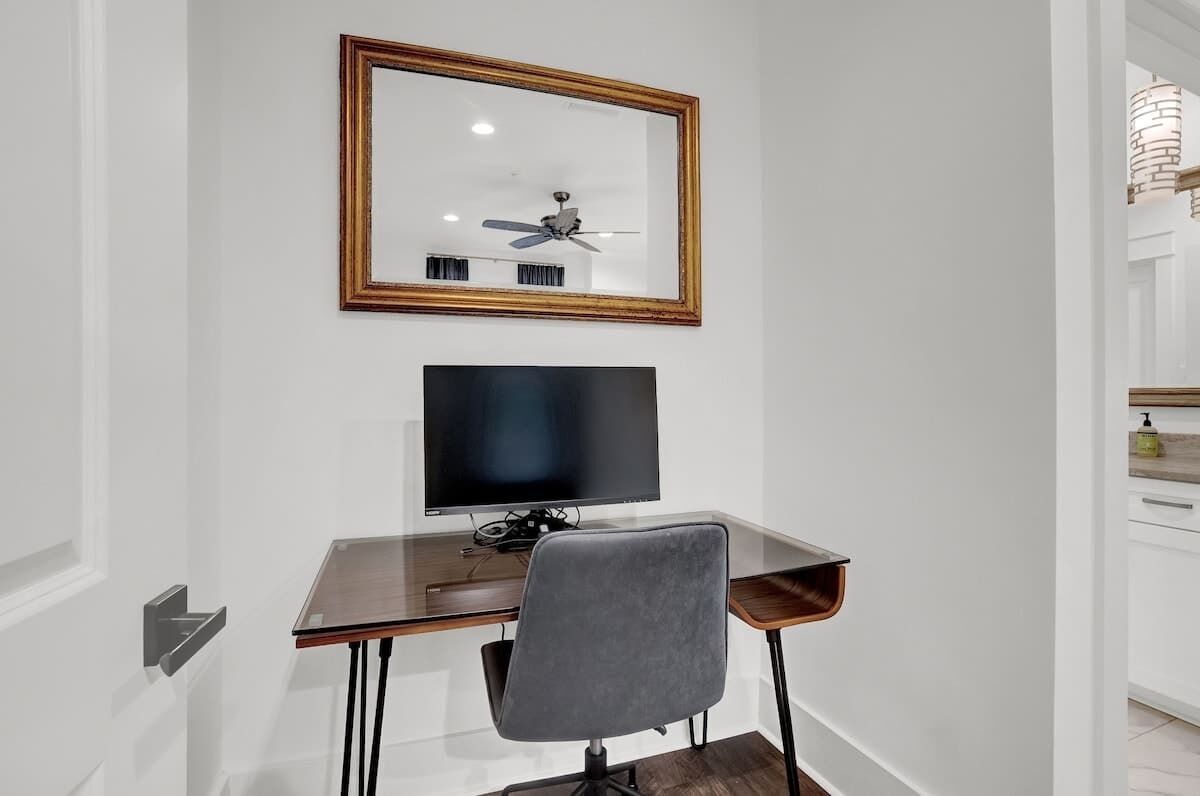 Een moderne kamer met een houten bureau, een zwart beeldscherm, een grijze stoel en een plafondventilator.